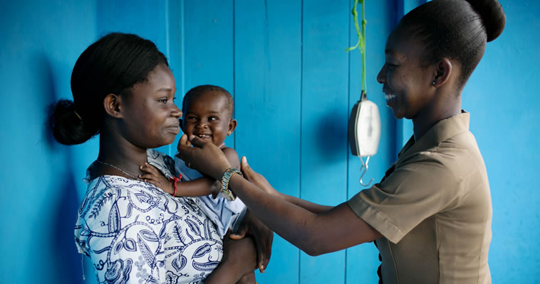 A young mother and her child are tested by a smiling health worker. Photo credit: Kate Holt for JHPIEGO/the USAID/Ghana Maternal and Child Survival Project