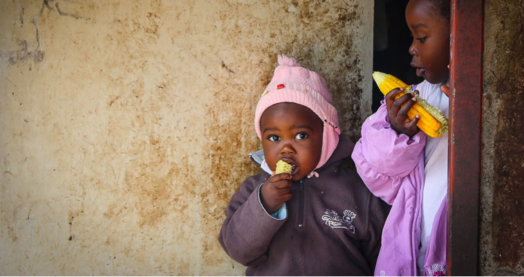 Two young Zambian girls eat maize. Photo credit: Chando Mapoma, USAID
