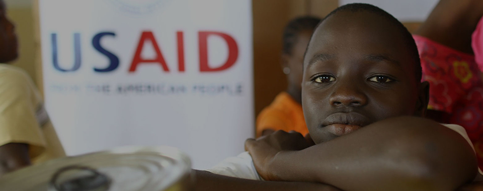 a boy sits in front of a USAID banner