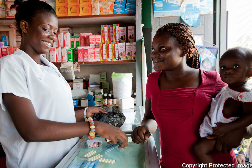 A woman holds her child while speaking to a pharmacist