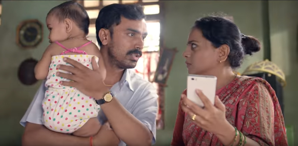 A man holds a child while speaking to a woman holding a phone