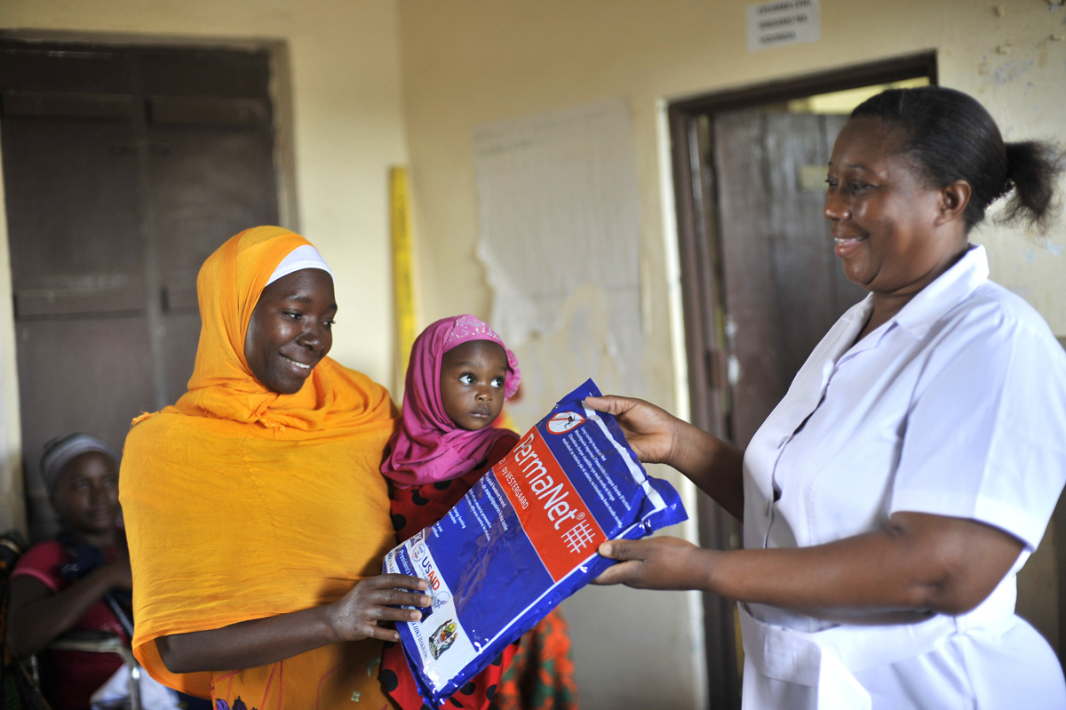 A health worker hands a mosquito net to a mother