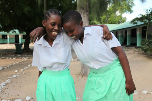 Two young girls laugh and throw their arms around each other.