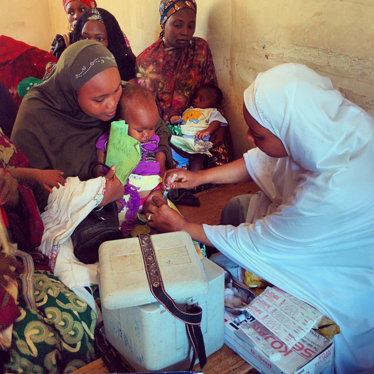 Nigerian women hold their young children while they are getting polio vaccinations.
