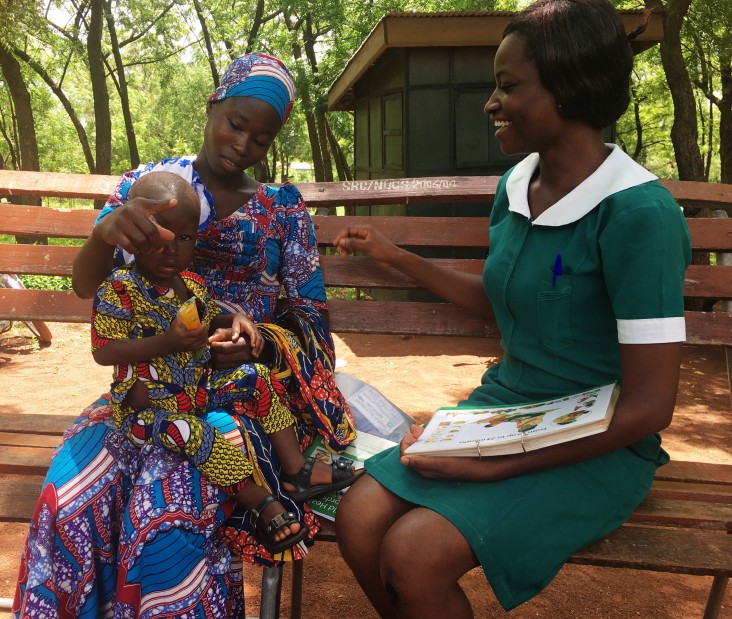 A Ghana health worker discusses breastfeeding with a woman holding a young child.