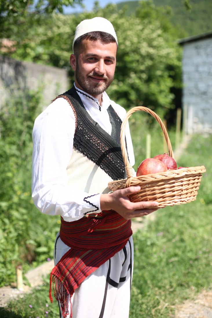 A young man dressed in traditional clothes holds a basket of pomegranites