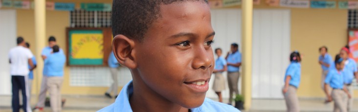 A boy, whilst in school, looks at the right with a smile.