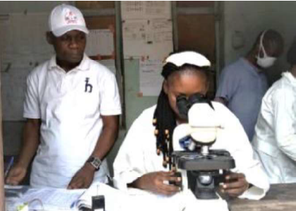 A health care worker looks into a microscope