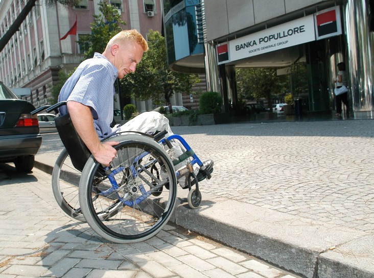 A young man in a wheelchair accessing a sidewalk without a wheelchair ramp