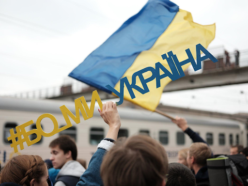 A person holds a sign "#Because we are Ukraine"