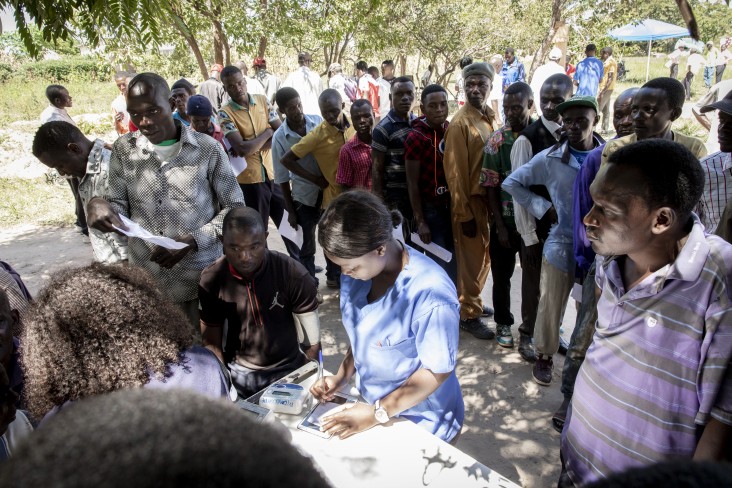 A group of men wait to receive a medical screening from a nurse.