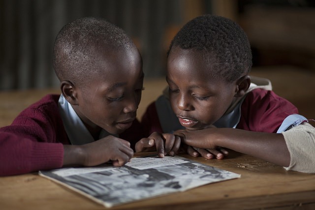 Two Kenyan boys read together while sharing a book.