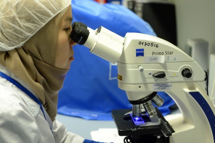 A health scientist focusing on tuberculosis looks through a microscope