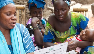 A health workers shares information with two women, one of whom is holding a baby.
