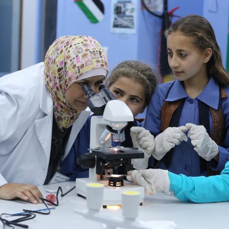 A science teacher looks through a telescope while two schoolgirls look on. 