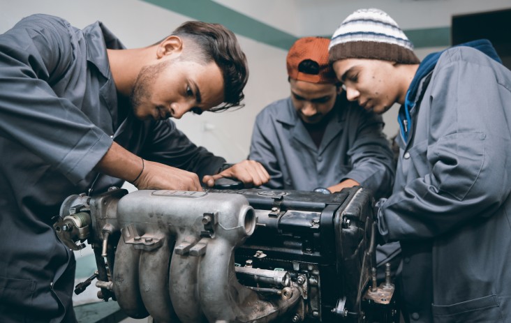 Three young men work on a car engine. 