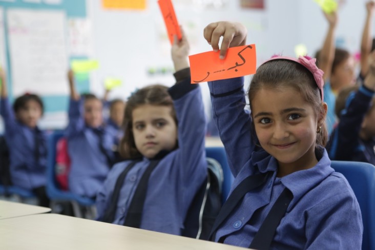 A schoolgirl holds up a paper that says "big" in Arabic. 