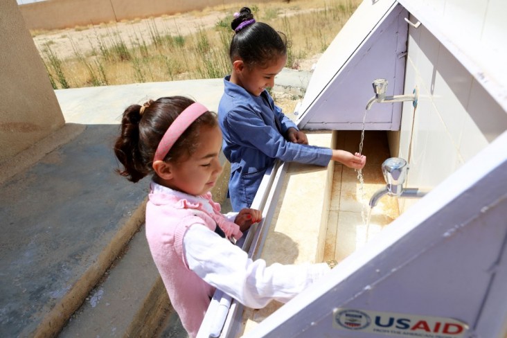 Two girls wash their hands at a USAID-branded school washbasin.