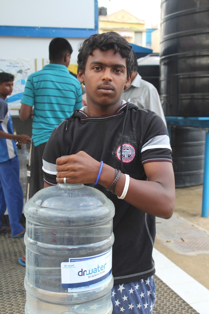 A resident of Lingarajpuram holds a 20-liter can of purified water.
