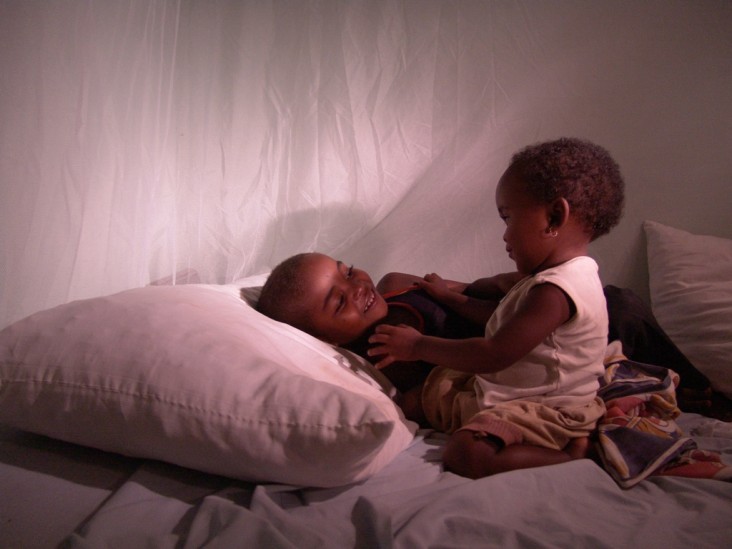 Two children sit under a bednet