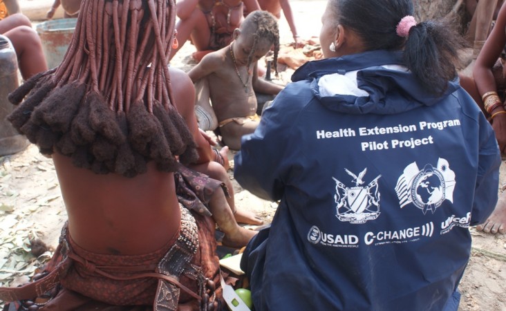 A woman wearing a C-CHANGE jacket sits with a group of women and children.