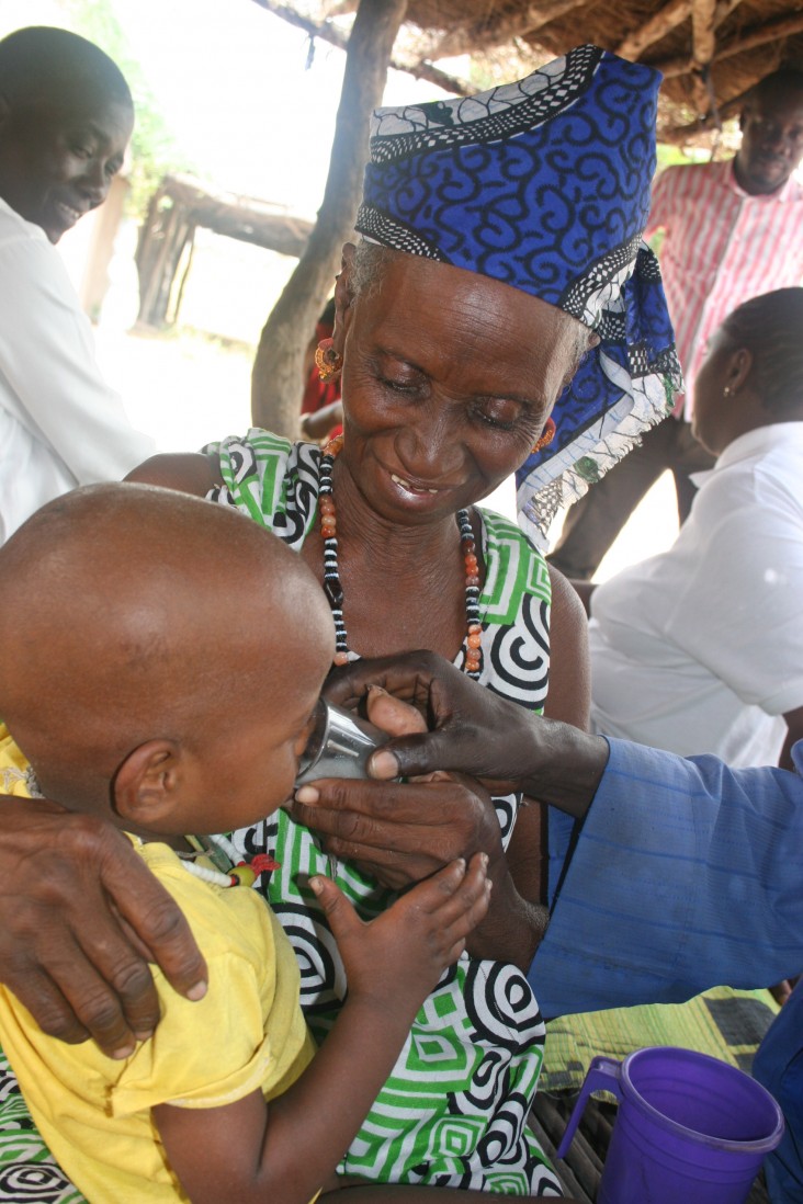Rougui Diallo holds her son as he drinks malaria prevention medicine.