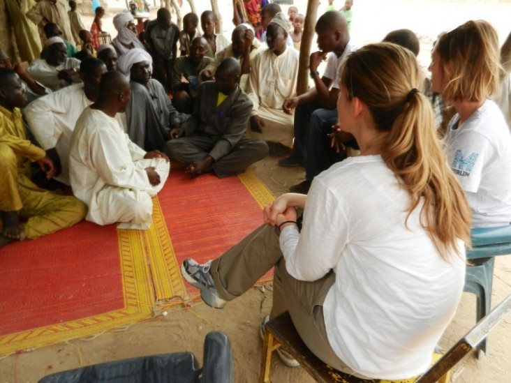 A USAID/OFDA staff member (foreground) meets with a men’s group in Chad while conducting a field visit 