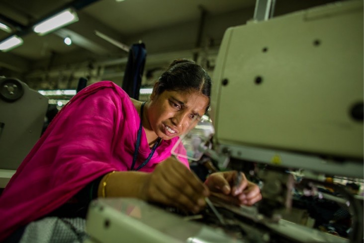 Shahara, a garment worker in Bangladesh, stitches buttons on blazers at her workstation in a garments factory in Gazipur, Dhaka. / Josh Estey, USAID