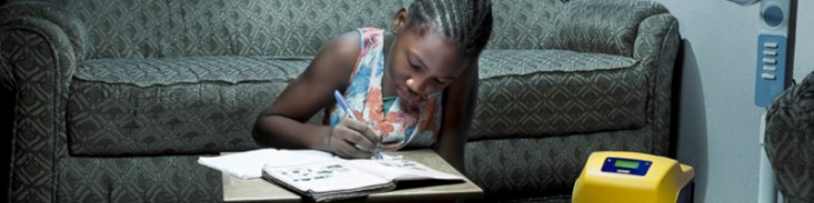 A young girl in Nigeria does her homework by the light provided by a Lumos Solar Power Station, an off-grid solar-power solution