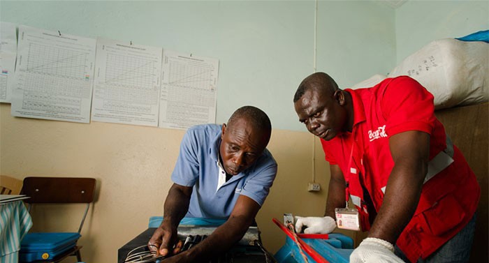 Two men work on fixing a refrigerator at a clinic