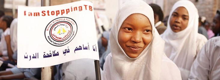 A woman wearing a white head scarf holds up a sign about TB.