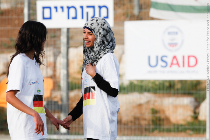 Two girls smiling at each other and holding hands after a USAID-supported day of peacebuilding activities that brings together Arab, Jewish, Israeli, and Palestinian girls in Kiryat Gat, Israel. 