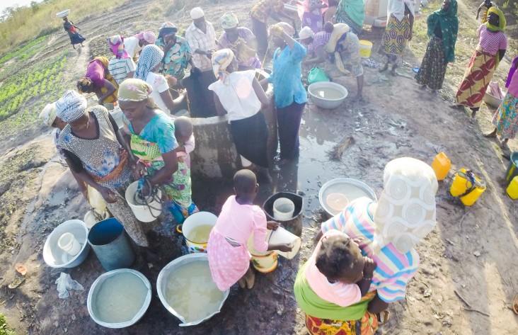 Women work together to collect water from a well for their community in northern Ghana.