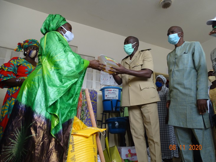Ms. Elise Sophie Sagna, USAID/Saabuñinmaa coordinator, symbolically handing a bottle of vegetable oil to the Sub-Prefect of Niaguis as the Mayor of Adeane, Ibrahima Diedhiou, looks on