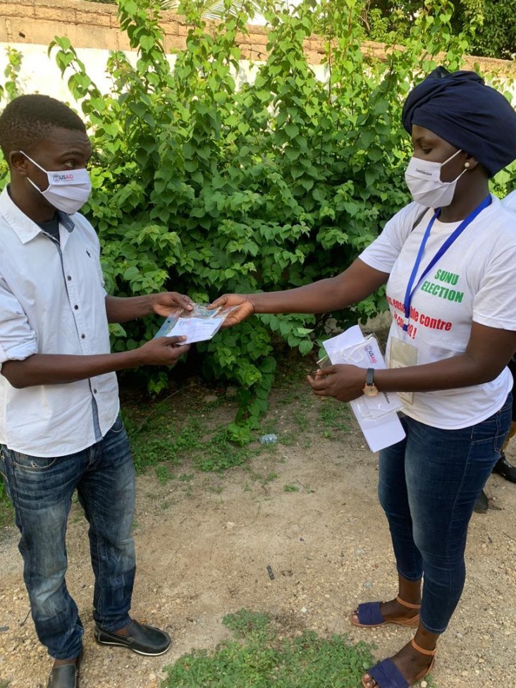 A community relay part of the Xeex Corona team giving a reusable mask to a youth after explaining the barrier measures. SunuElection, USAID