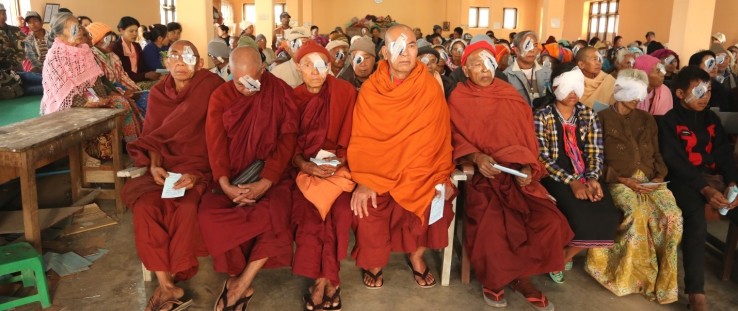 Monks sit among a group of people waiting to remove their bandages following cataract surgery.