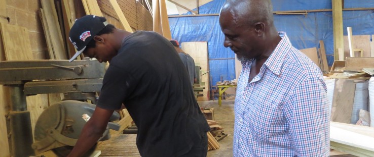 Tre Espirit uses the USAID-funded radial arm saw under the watchful gaze of his teacher, master craftsman John Riviere.