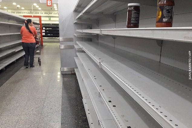 A woman walks between the empty shelves of a supermarket in Caracas, Venezuela.