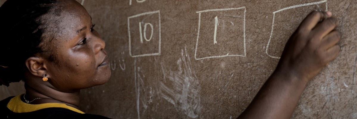 A woman writes on a chalkboard. Photo by Neil Brandvold, USAID