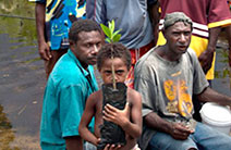 A boy holding a mangrove poses for the camera while standing in front of residents of his village